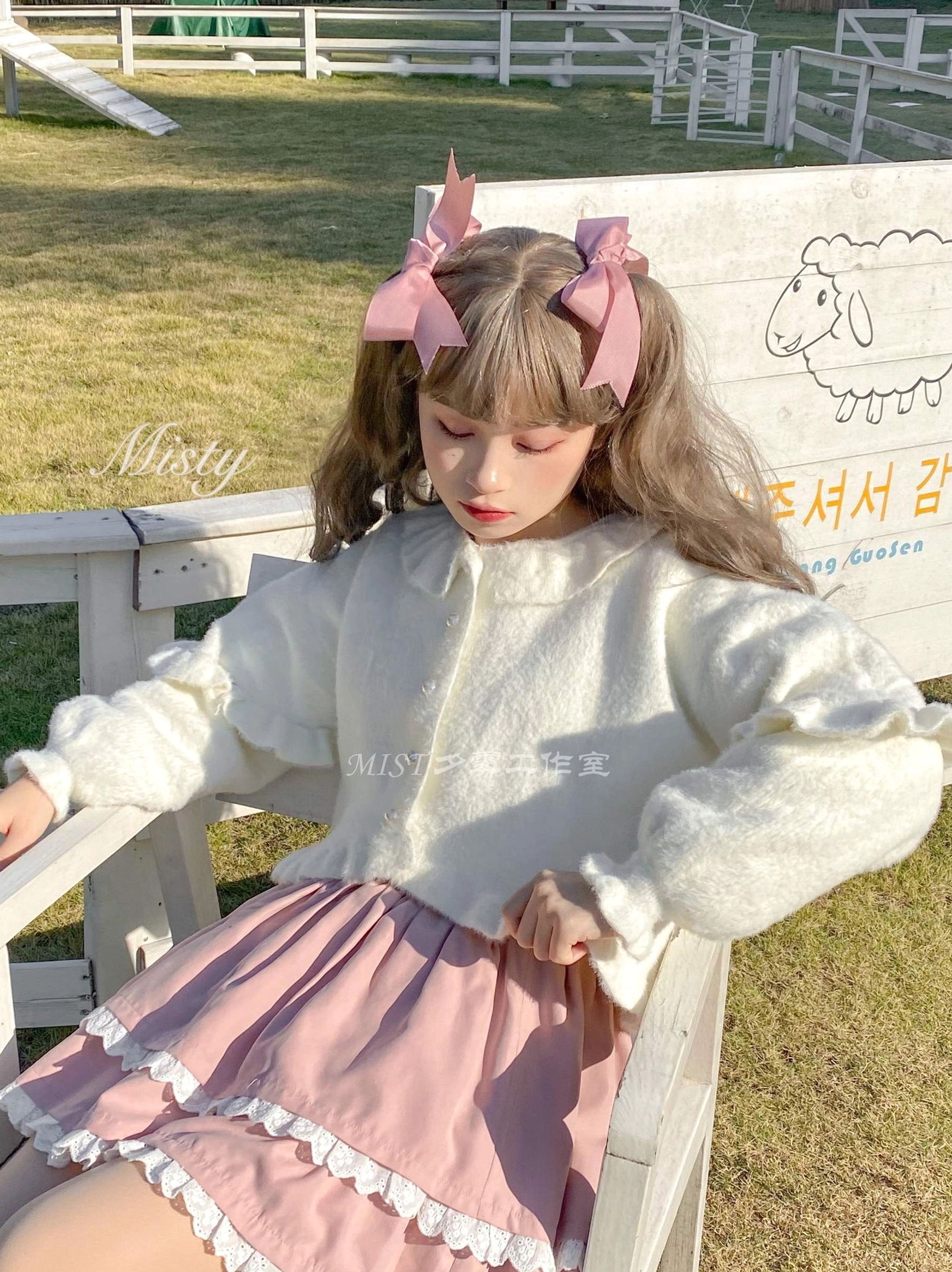 White fuzzy sweet lolita cardigan pink skirt three-quarter seated side view ruffled sleeve cuffs lace-trimmed mini skirt pasture setting