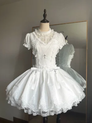 White Gothic Lolita OP dress front view on mannequin displaying puffed short sleeves, sheer lace stand collar, detachable cross ornaments, and lace-trimmed flared mini skirt with waist bows, shown in fitting room with gold-framed mirror