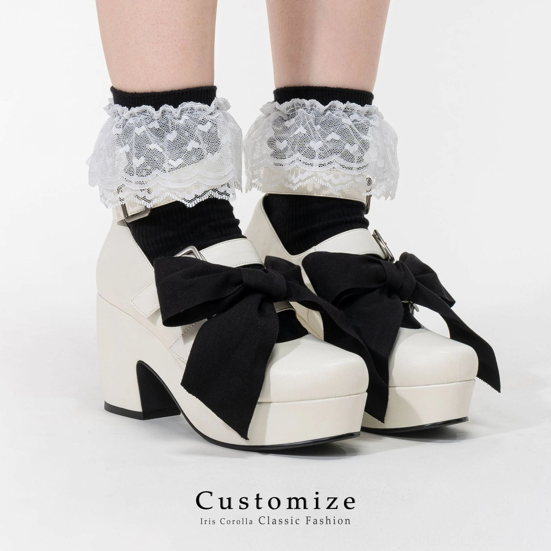 White Gothic Lolita platform heel shoes with large black detachable bow, black lace-trimmed ruffled crew socks, chunky block heel, silver buckle straps, front oblique view model feet