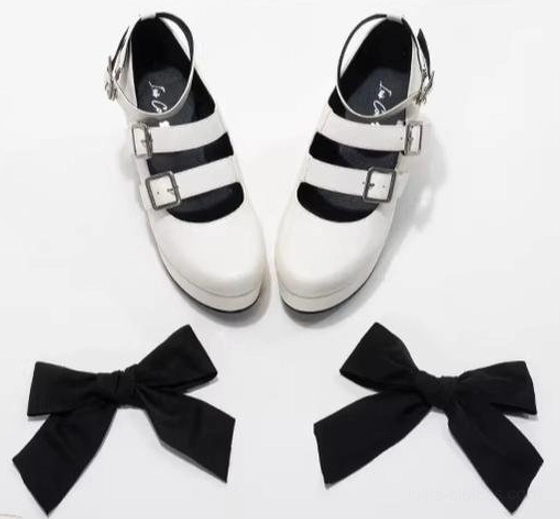 White Gothic Lolita platform heel shoes and pair of detachable large black fabric bows flat lay display plain white background, two silver buckle straps, smooth white leather material