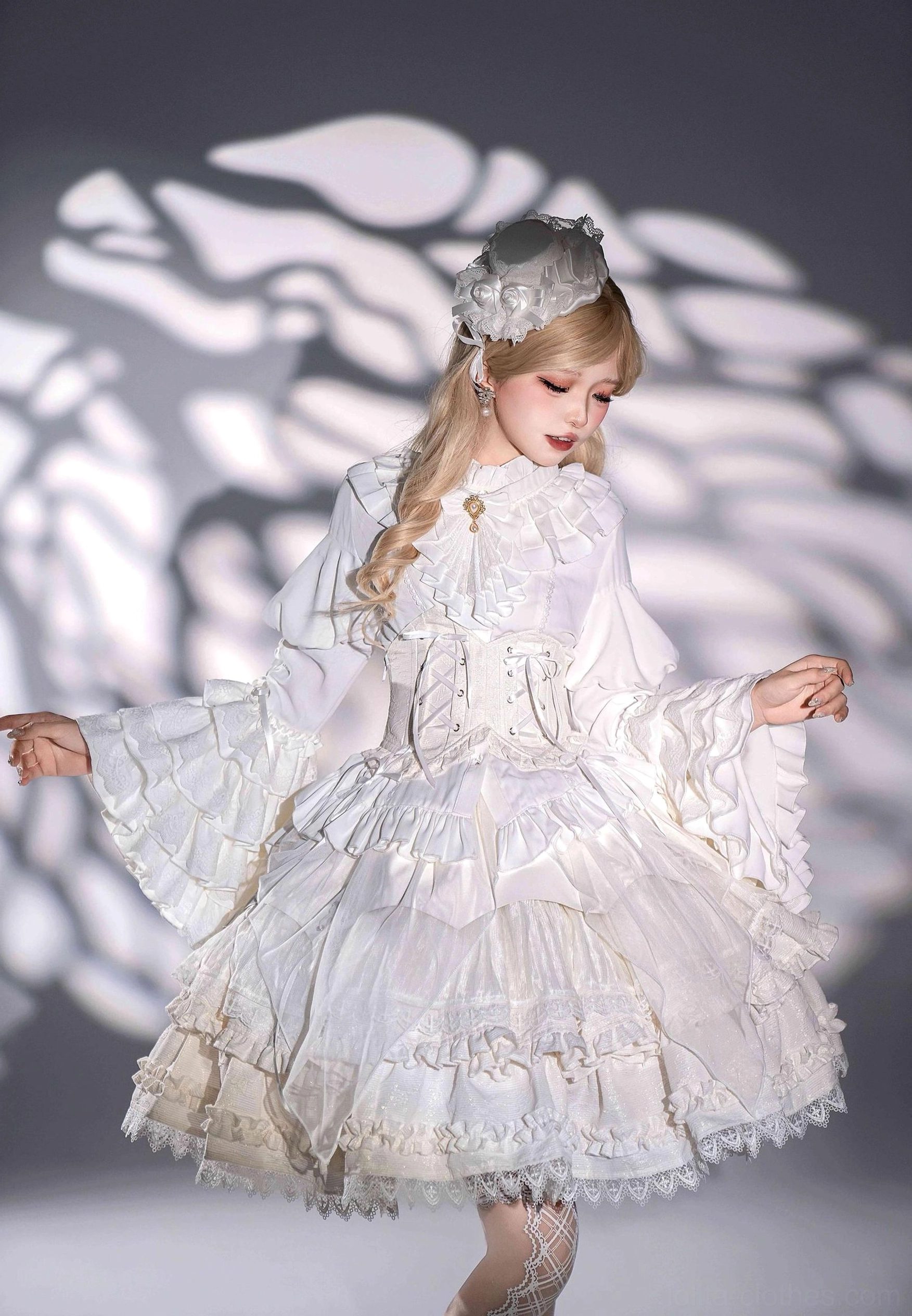 Half-body front pose of model wearing white gothic lolita dress showing large flared bell sleeves ruffled tiered skirt fitted corset waist and lace headdress accessory