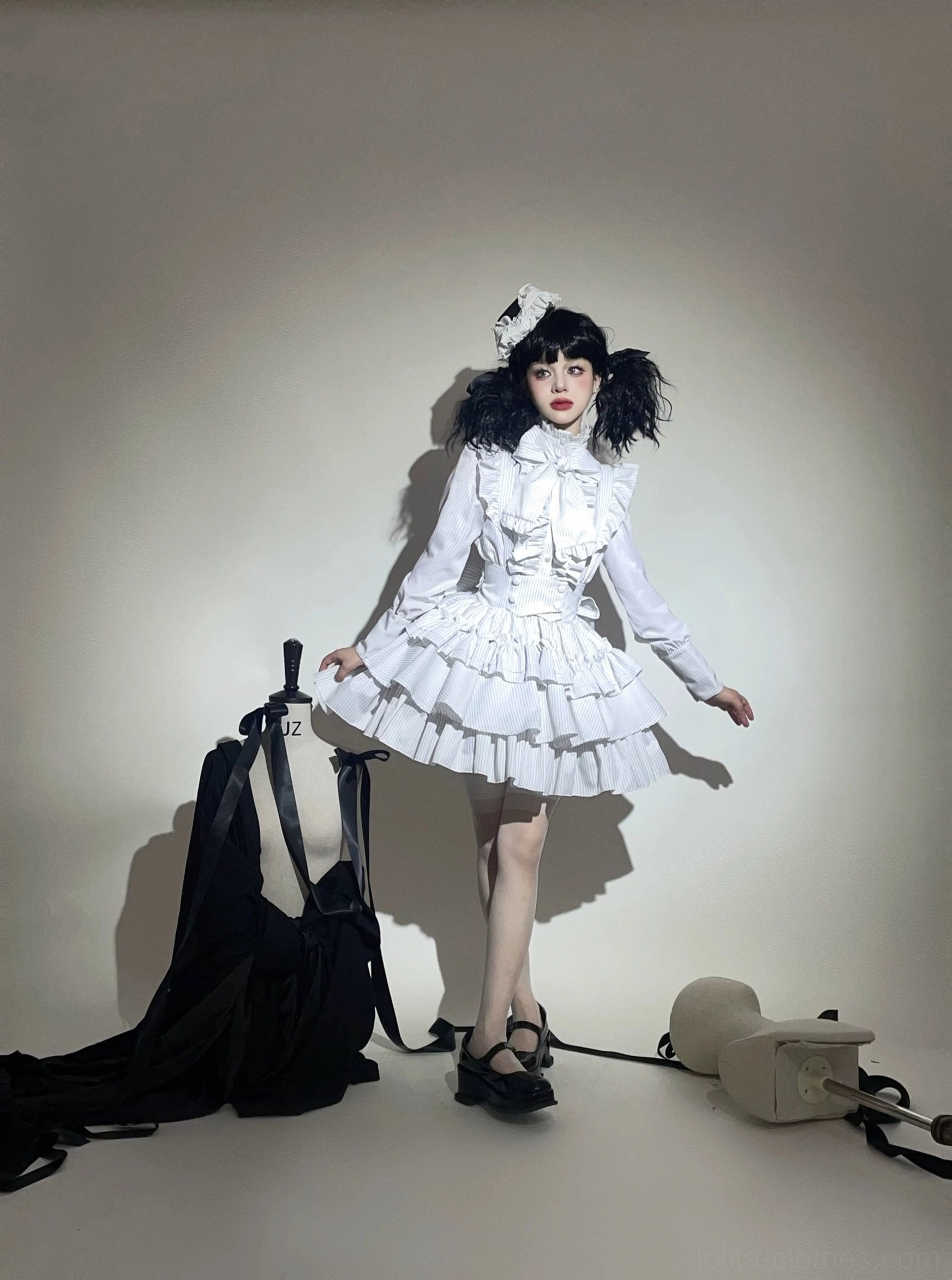 White gothic lolita two-piece striped set on standing model in three-quarter front angle, showcasing multi-layered ruffled mini skirt, long puff sleeves, bow neck decoration