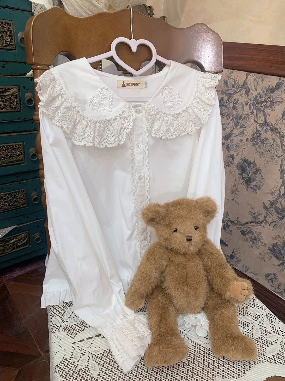white sweet lolita long-sleeve cotton blouse with ruffled lace collar hung on heart-shaped hanger vintage chair teddy bear