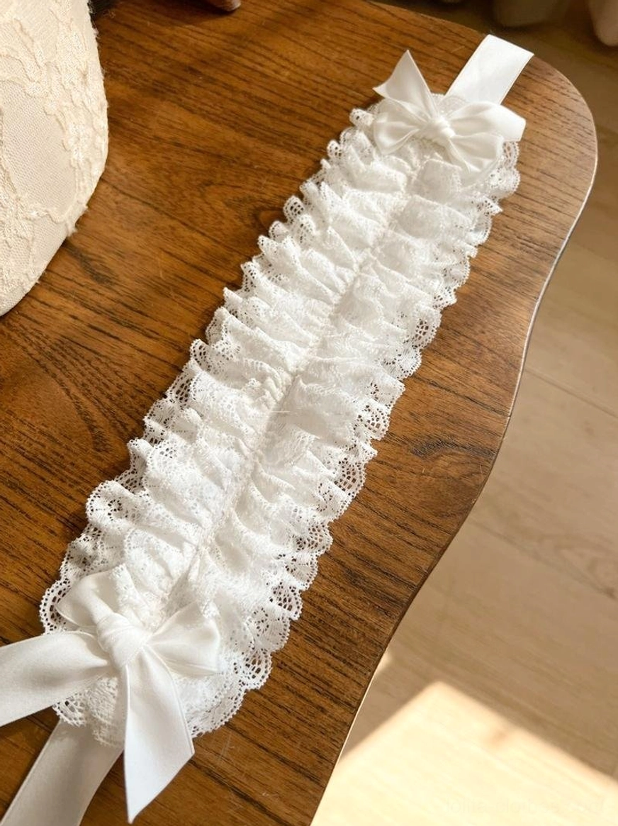 White ruffled lace KC headdress flat lay overhead shot on wooden surface, displaying white satin bows at both ends and long matching ribbon straps