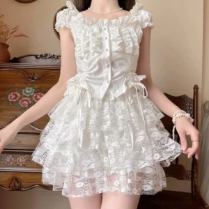 White lace lolita bloomers with tiered ruffled hem worn by model in front view, displaying square neckline ruffled top and layered lace shorts against vintage floral dresser