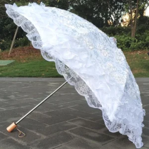 White lace Lolita sun parasol with tiered ruffled lace trim and wrist strap handle photographed outdoors in garden patio setting with green plants background
