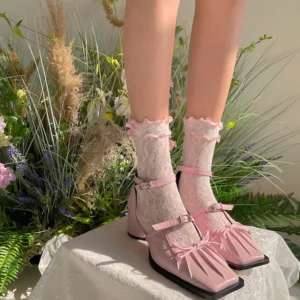 Delicate white sheer lace Lolita ankle socks with pink ribbon bow paired with pink square-toe Mary Jane shoes displayed on model's feet with floral greenery background