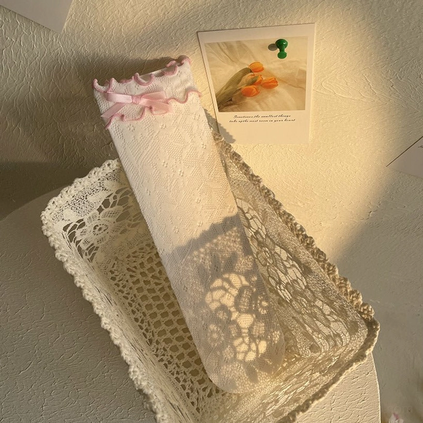 White delicate floral lace Lolita ankle socks with pink ribbon bow and ruffled cuff displayed on model's leg showing sheer lace construction