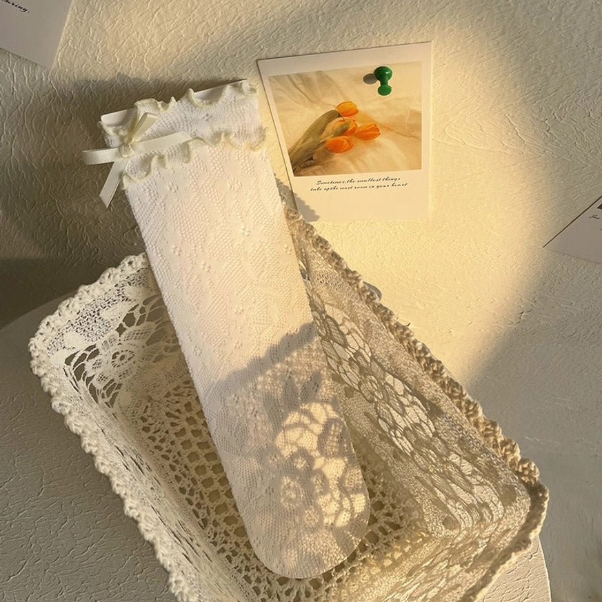 White delicate lace Lolita ankle socks with yellowish ribbon bow accent displayed on model's leg showing sheer floral pattern and ruffled cuff detail