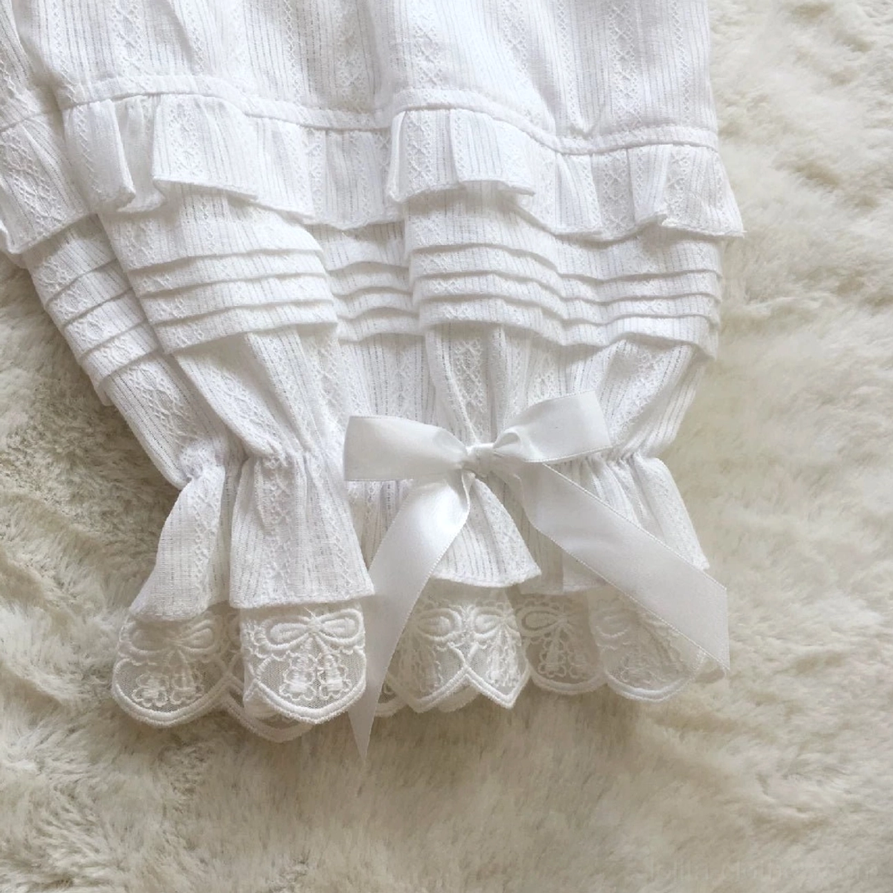 Close-up detail flat lay side view of white sweet lolita bloomers cuff showing accordion fabric pleats satin bow decoration embroidered lace hem textured jacquard cotton