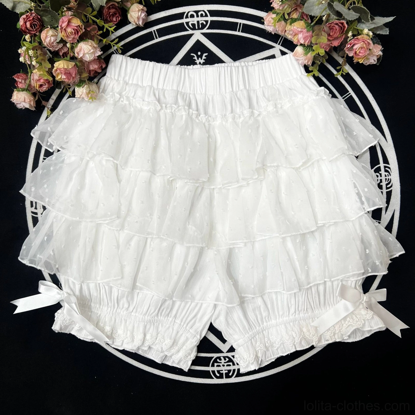 White layered lolita bloomers with multi-tier ruffled leg design featuring satin bow embellishments on flat lay display with floral background