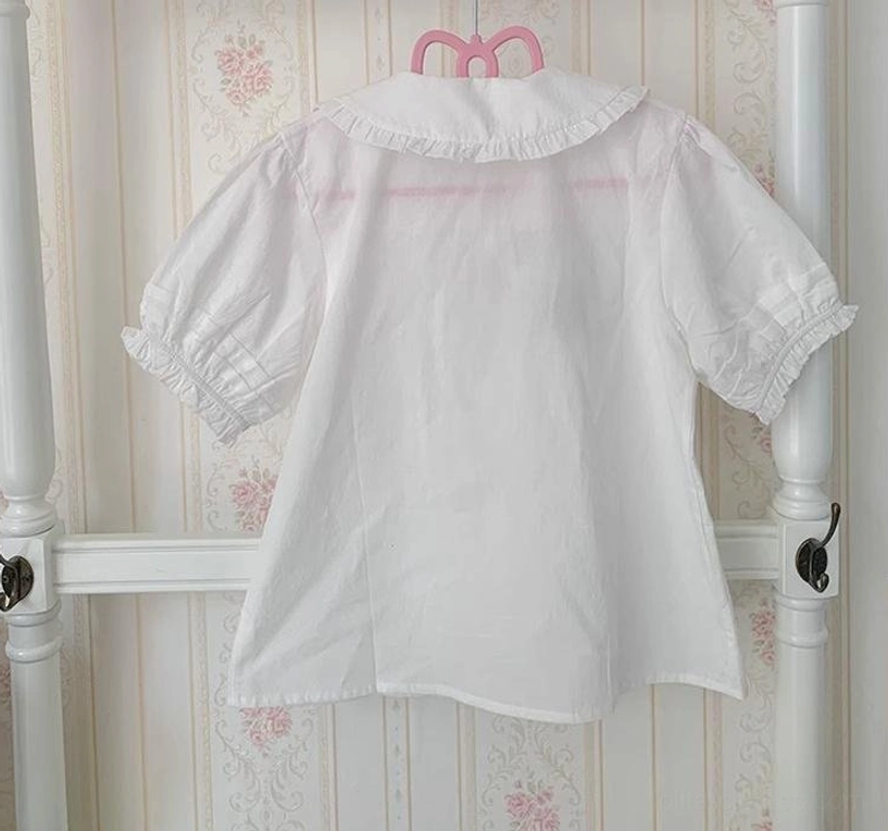 White cotton lolita blouse back view showing simple unadorned back design, ruffled puff sleeves and solid white fabric on hanger with vintage background