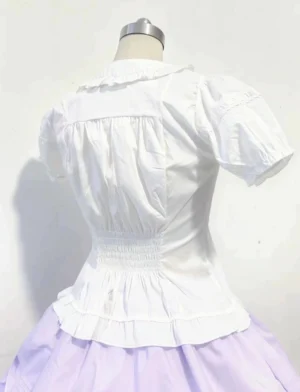 Back view of white sweet lolita blouse featuring shirred waist panel and ruffled hemline, displayed on dress form with light purple tiered skirt, showing short puff sleeves and back silhouette