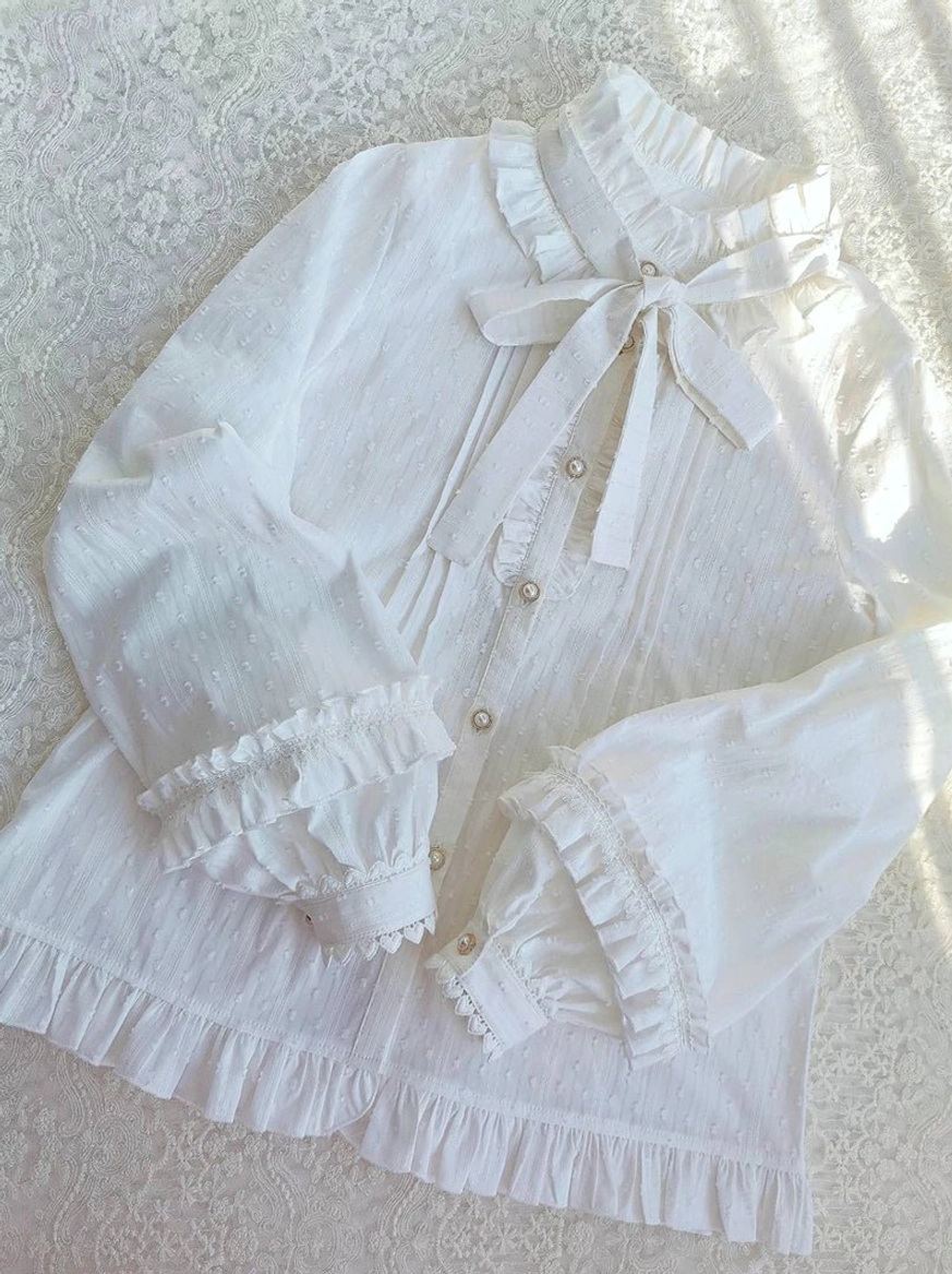 White lolita blouse flat lay overhead view ruffled collar detachable bow tie pearl button front closure lace background