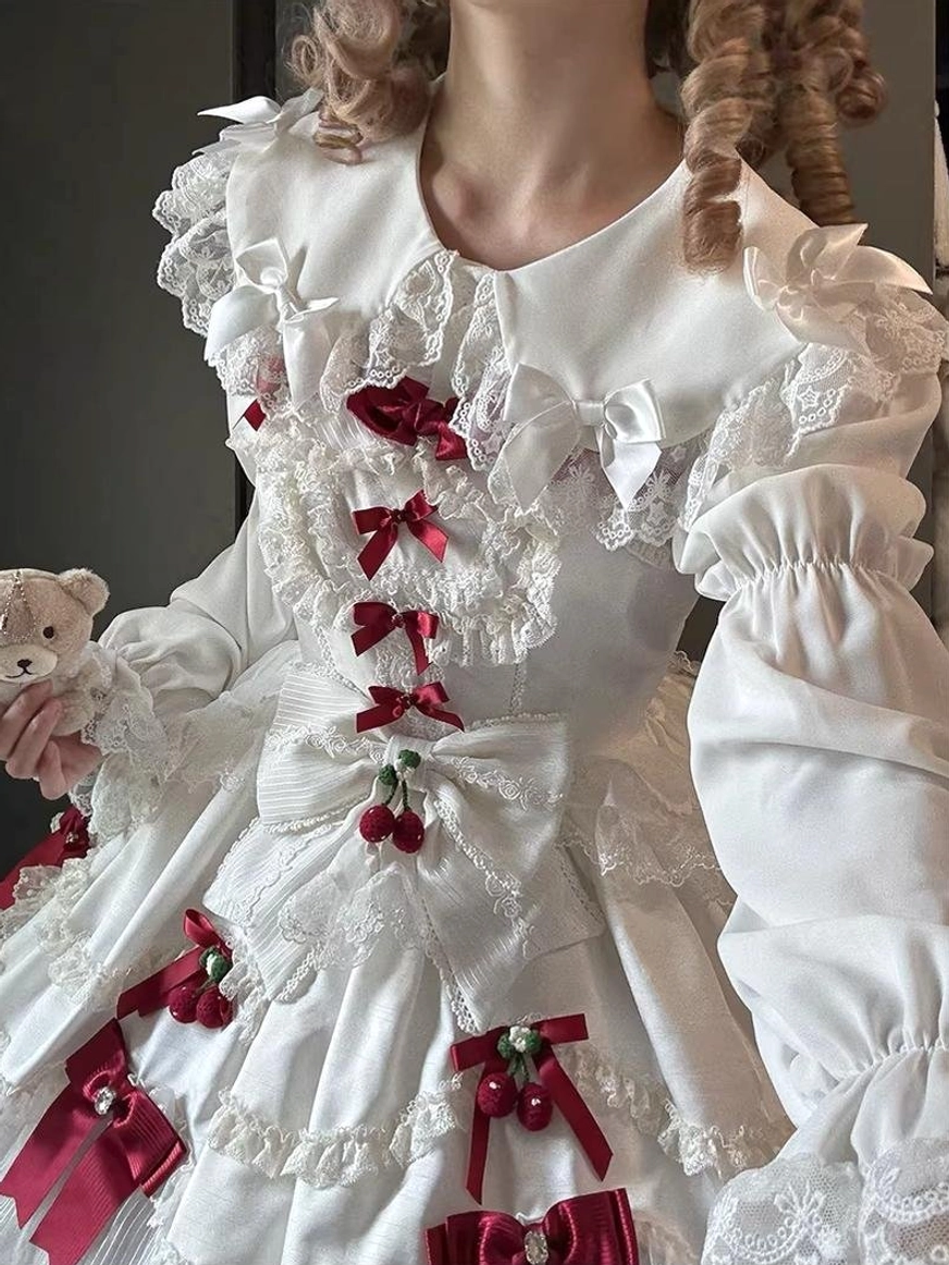Three-quarter front close-up of white Lolita blouse and bodice showing puffed ruffled sleeves, front red bow lacing, and detailed lace collar worn by curly-haired model