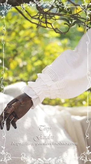 Close-up detail of ruffled cuff and pleated lantern sleeve on white doll collar lolita blouse wooden mannequin hand