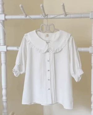 White short sleeve lolita blouse with ruffled doll collar and puffy silhouette hanging on decorative hanger studio product shot