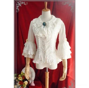 White ruffled classic Lolita blouse with lace Peter Pan collar, gem-set brooch, layered ruffle bell sleeves, and front button fastening on mannequin