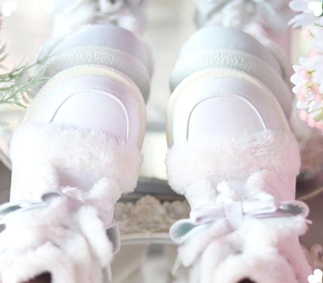Pair of white lolita winter boots overhead close-up on mirror tabletop with floral accents, showing fluffy plush trim and smooth leather surface