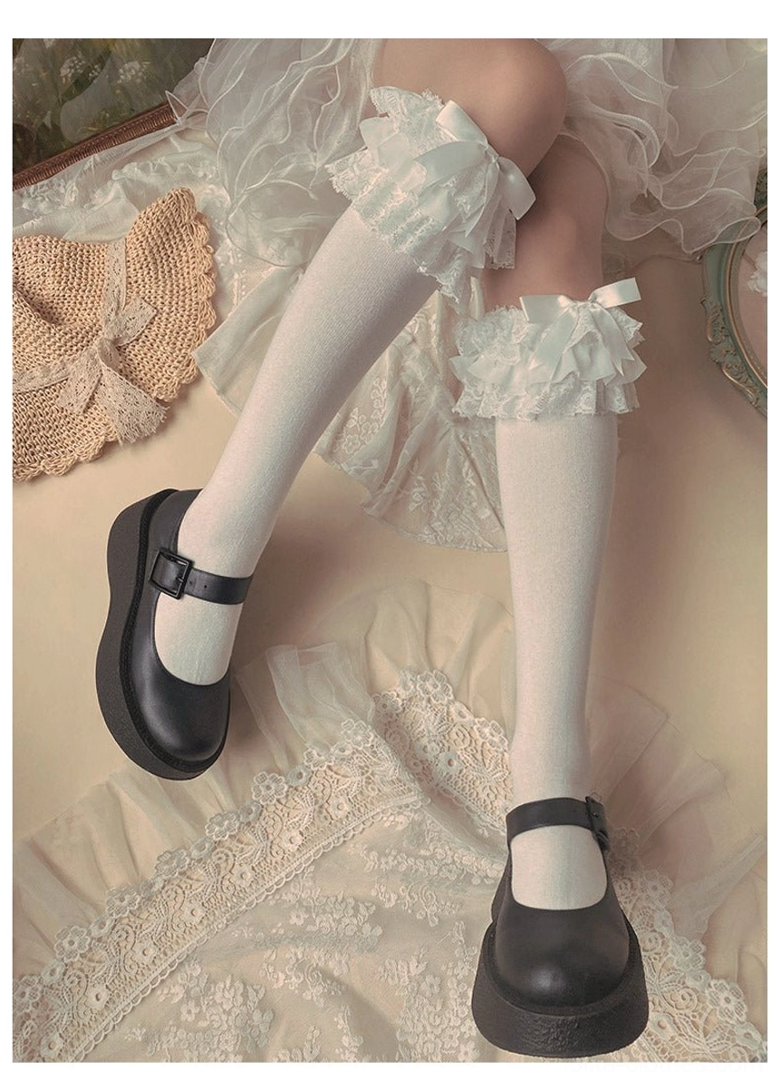 White cotton Lolita mid-calf socks low side view with ruffled lace trim cuff small white bow black Mary Jane shoes lace cloth background