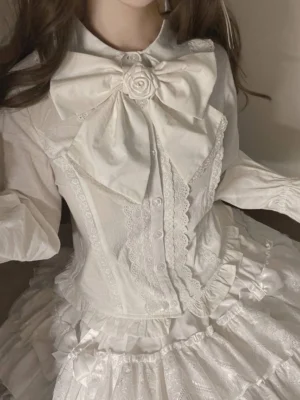 White kawaii lolita blouse with bubble puff sleeves and tiered ruffle skirt set, close-up front view showing lace collar and rose bow ornament detail on upper body
