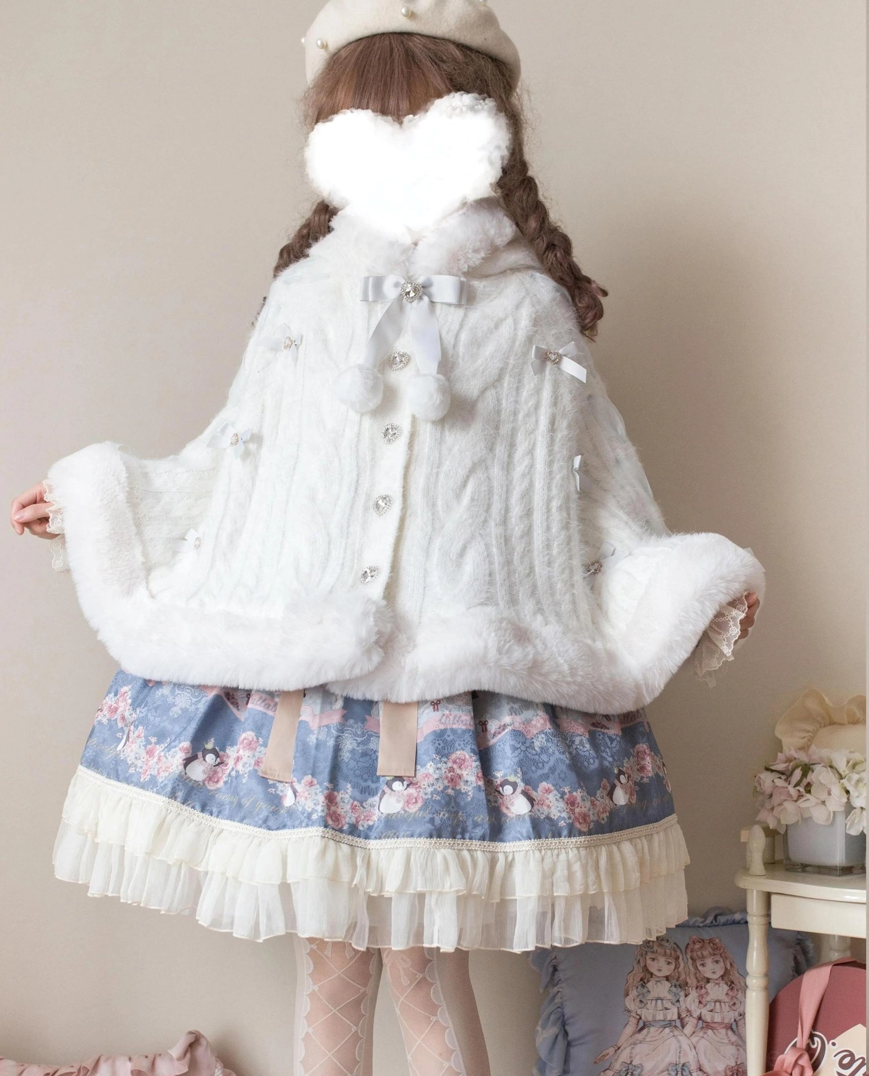 White faux fur lolita winter cape coat back three-quarter view with back bow collar, pom-pom decorations, button front closure, wide plush fur trim edges, blue cartoon-print skirt