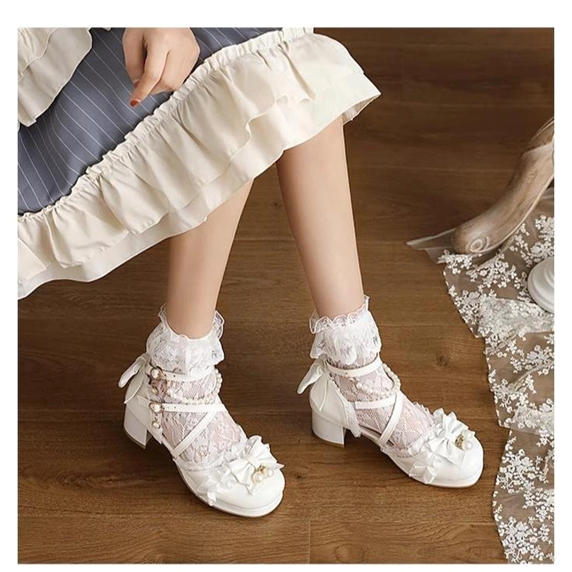 Flat overhead view of white Lolita dress sandals with ruffled lace socks bow embellishments closed round toe chunky heel on wooden floor with lace tablecloth decor