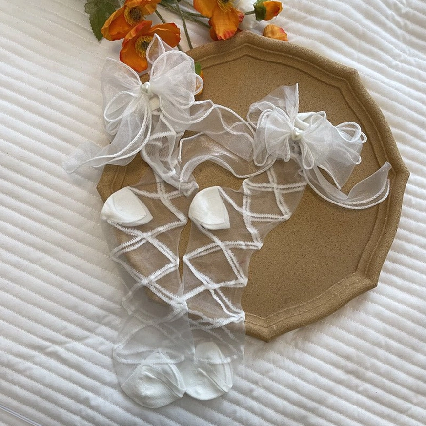 Top-down flat lay of white lolita gauze leg wraps with dual organza bows and heart details featuring sheer crisscross straps on decorative tray with linen mat and flowers
