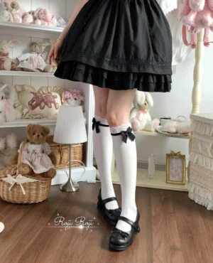 White lolita knee-high socks with lace cuff trim and black bow detail worn with black Mary Jane shoes and black short lolita skirt back view