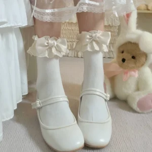 White Lolita lace bow crew socks with beige bow accent paired with white Mary Jane shoes, worn on model's feet in sweet princess indoor setting with teddy bear prop and lace decor