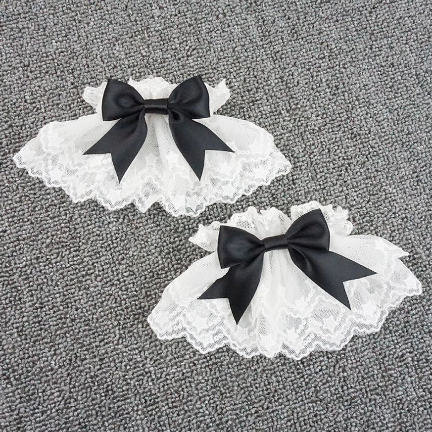 Sweet lolita wrist cuffs white pair flat lay with scalloped lace trim and black satin bow ornament overhead view
