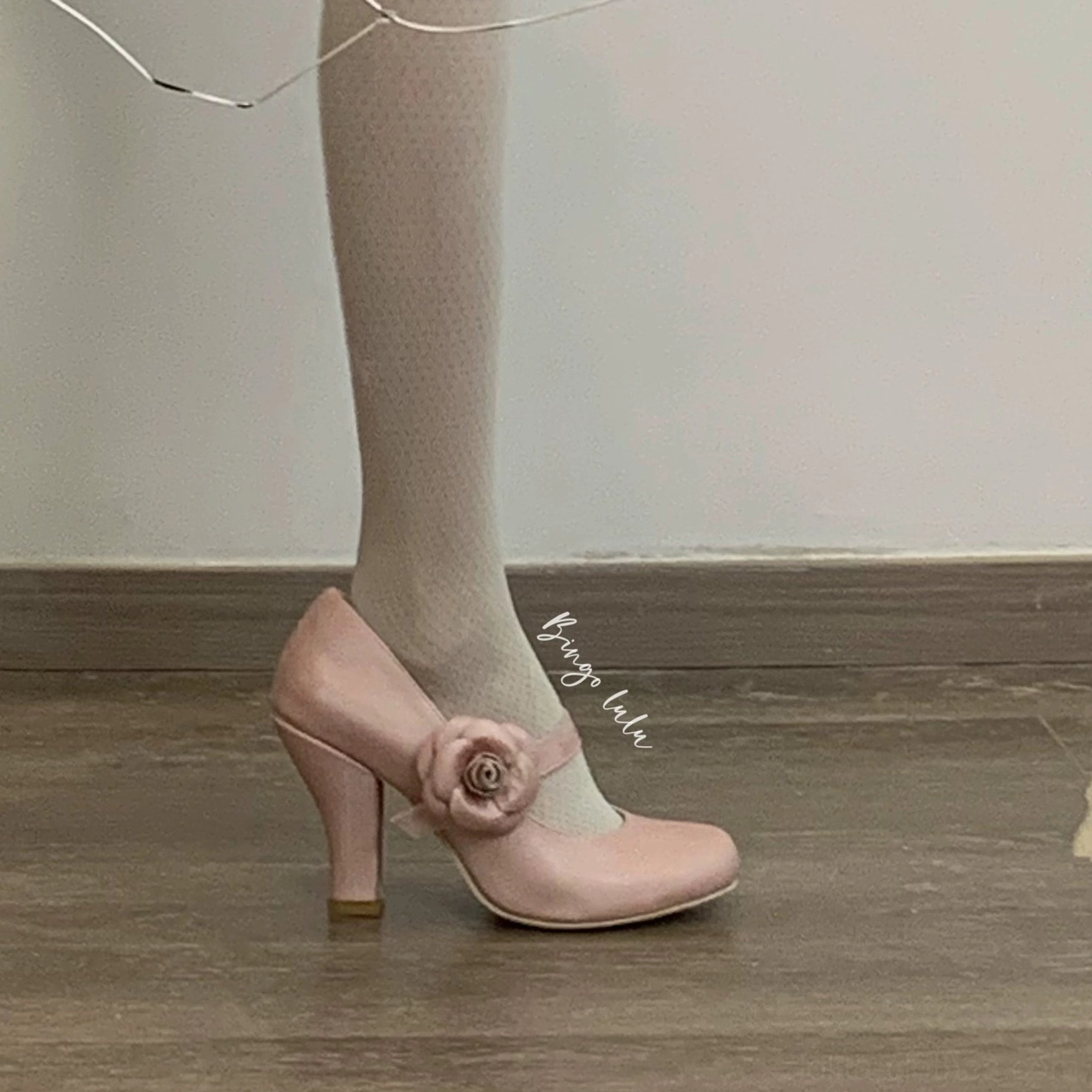 White Lolita Mary Jane high heel shoes side view of wearing feet indoor wooden floor fairy lights ruffled decorative frame patent leather white rose ankle strap sheer tights