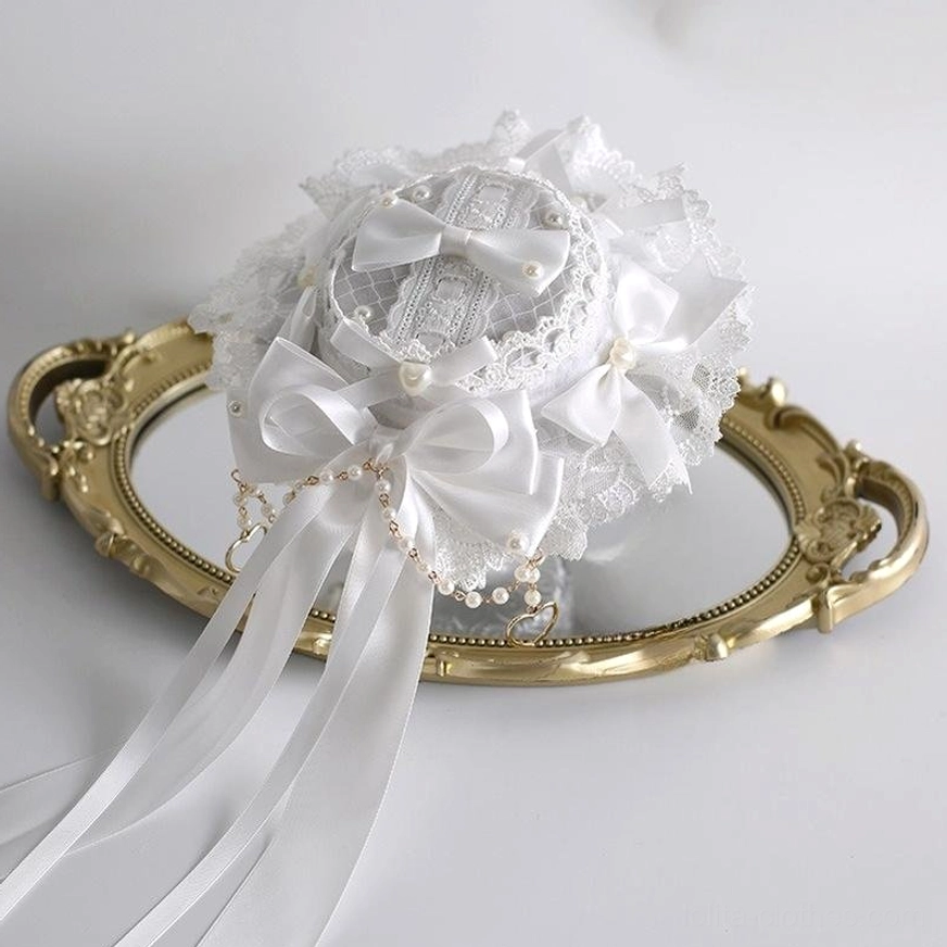 White lolita mini bonnet hair accessory with ruffled lace edges, large satin bow, pearl tassel trim flat lay vintage mirror