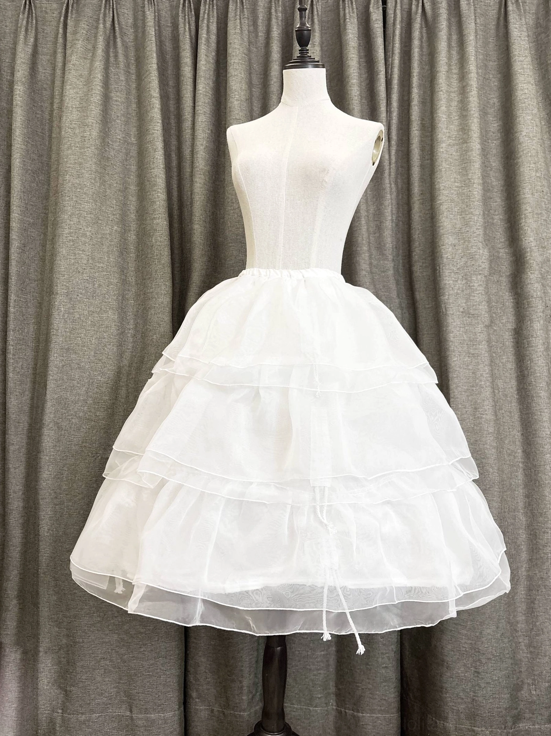 Front right diagonal view of white layered Lolita petticoat with visible drawstring adjustment at bottom hem and A-line silhouette