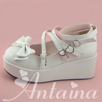 White Lolita platform shoes side three-quarter angle view on pink background displaying small toe bow, dual ankle straps with heart metal buckles, and flat thick platform sole