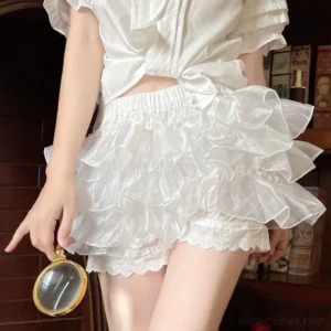 White lolita safety bloomers side lower-body close-up showcasing shiny multi-layer organza ruffle tiers with delicate lace hem paired with cropped white ruffled blouse in vintage study setting with decorative magnifying glass prop