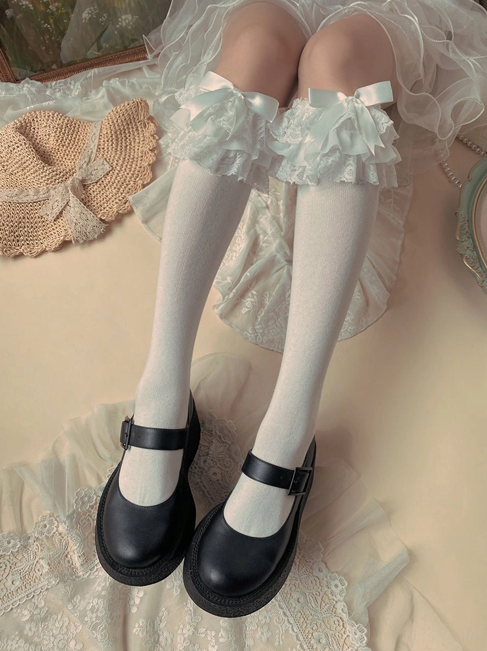 White cotton Lolita mid-calf socks overhead top-down view with white ruffled lace trim cuff and bow detail black Mary Jane shoes woven mat
