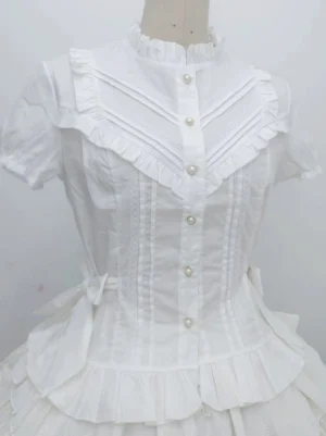 Close-up front detail of white Lolita blouse showing V-shaped ruffled bodice trim, vertical accordion pleats, full pearl button placket, and puffed short sleeves