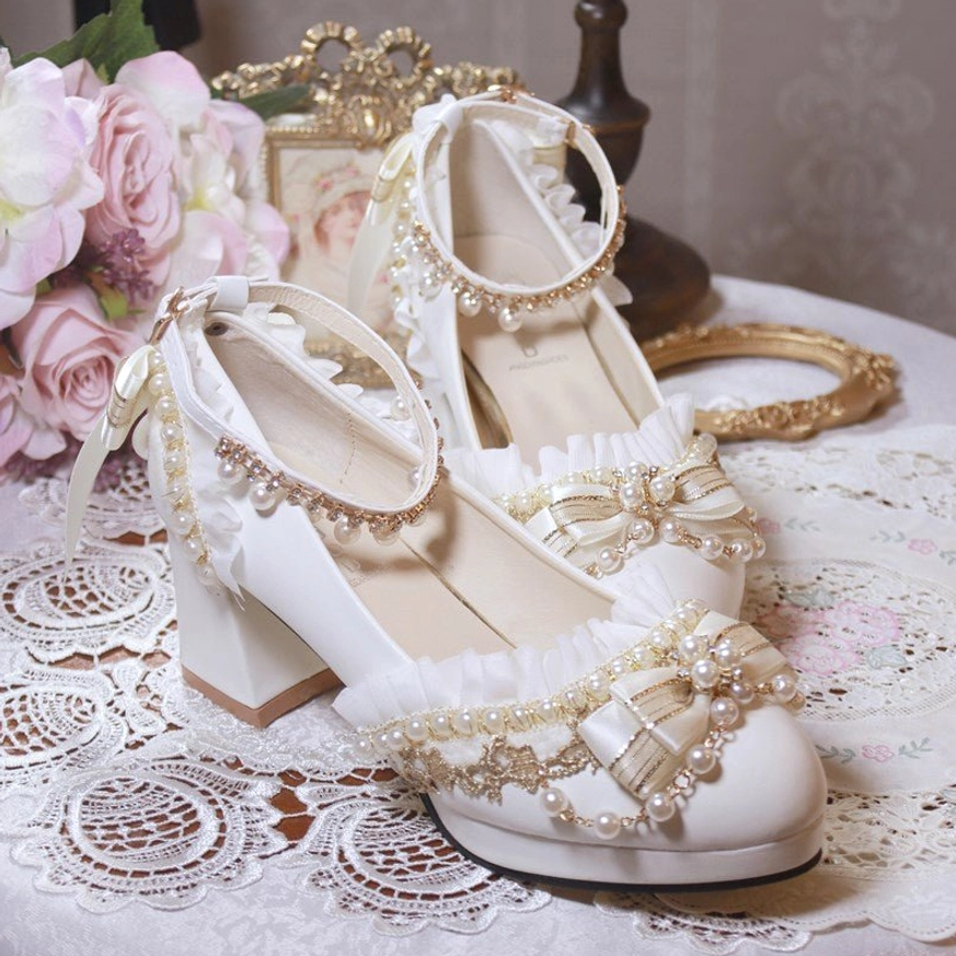 Handcrafted white bridal Lolita heel shoes side top view showing detailed vamp ruffled ankle strap and satin bow with pearl accents on lace-covered table