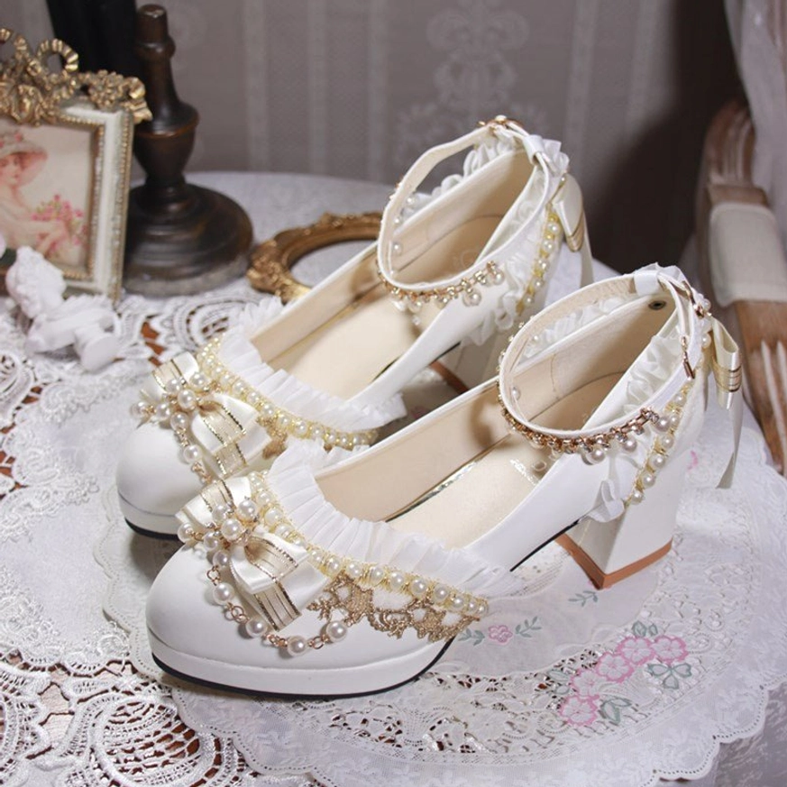 Handcrafted white Lolita wedding heel shoes three-quarter front view on vintage table with lace tablecloth retro decor showing chunky platform heel satin bows pearl embellishments