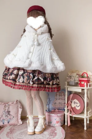 White faux fur lolita winter cape coat with cable knit texture, plush white fur trim, bow and pom-pom collar decorations shown on blurred-face model in vintage doll-themed setting