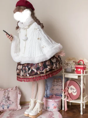 White faux fur lolita cape coat side three-quarter view with plush cuffs, hem pom-pom ornaments, paired with bear-print lolita skirt on model holding smartphone