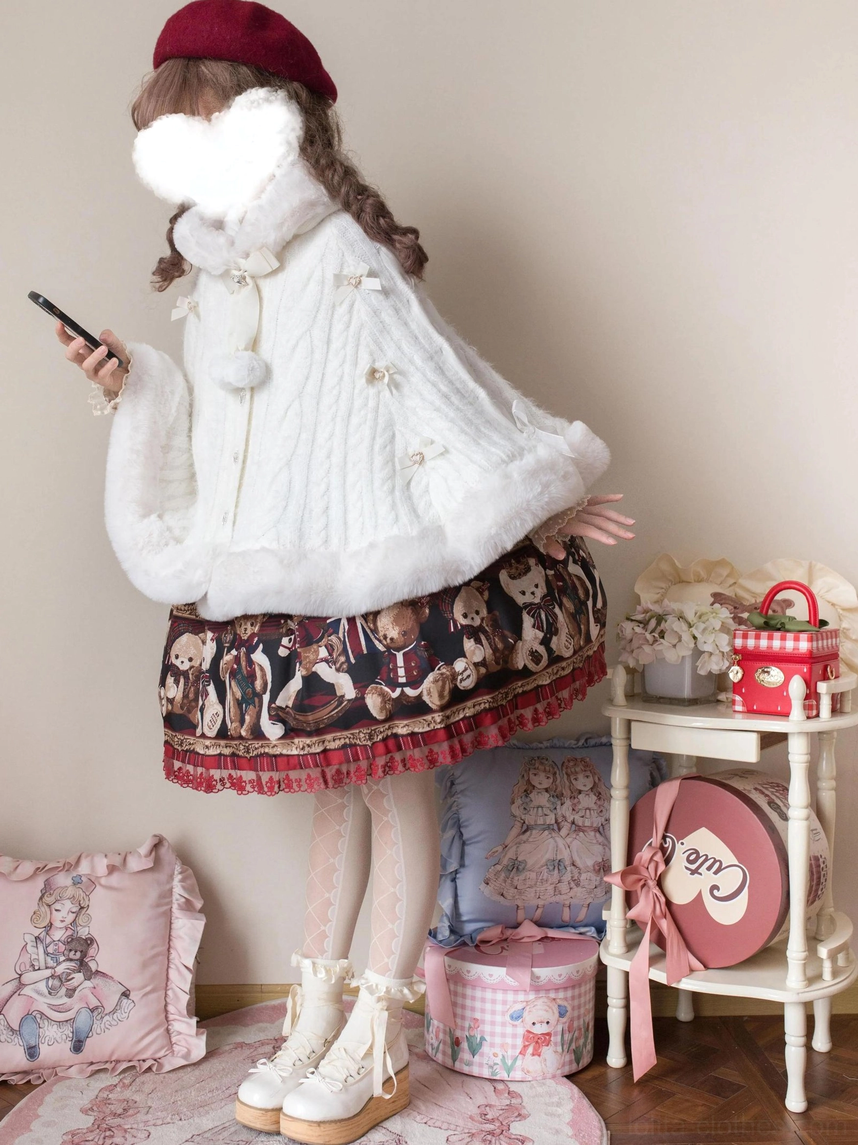 White faux fur lolita cape coat side three-quarter view with plush cuffs, hem pom-pom ornaments, paired with bear-print lolita skirt on model holding smartphone