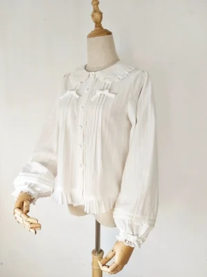 White long-sleeve sweet lolita blouse with ruffled lace collar, front pleats, bishop sleeves with ruffled cuffs, and decorative chest bows, three-quarter front view on mannequin