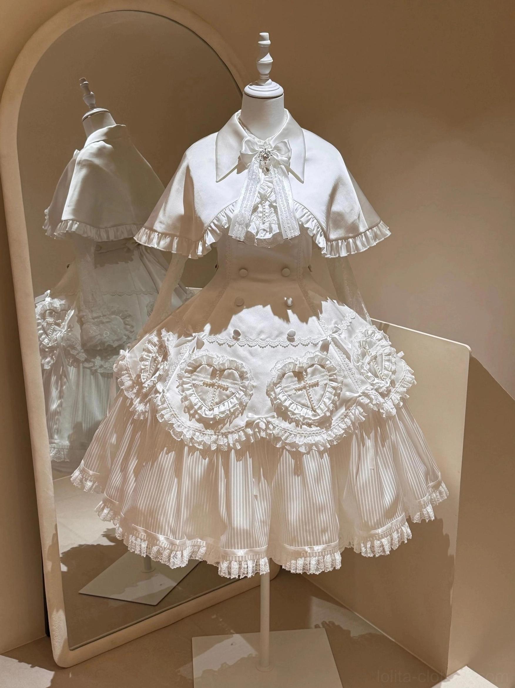 White Nocthymn Cross Gothic Lolita dress with matching capelet full-length mirror view showing satin fabric ruffled trims heart lace decorations pleated skirt layers
