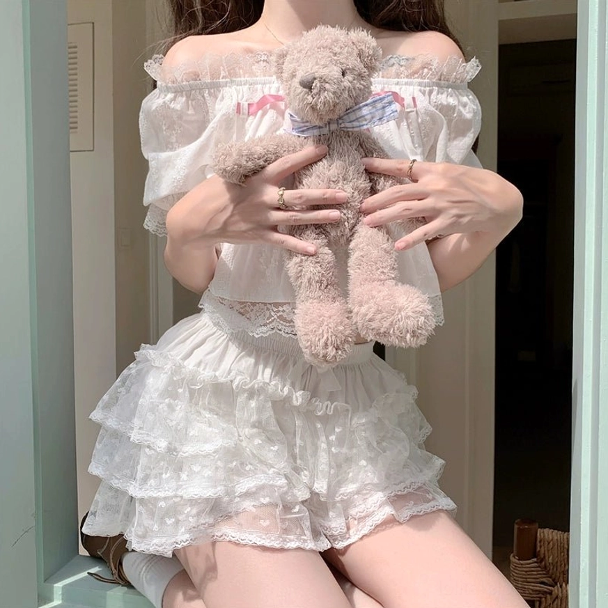 White off-shoulder Lolita two-piece set with pink chest bow, lace-trimmed puff sleeves, matching cropped top and bloomers worn by model sitting on windowsill holding teddy bear