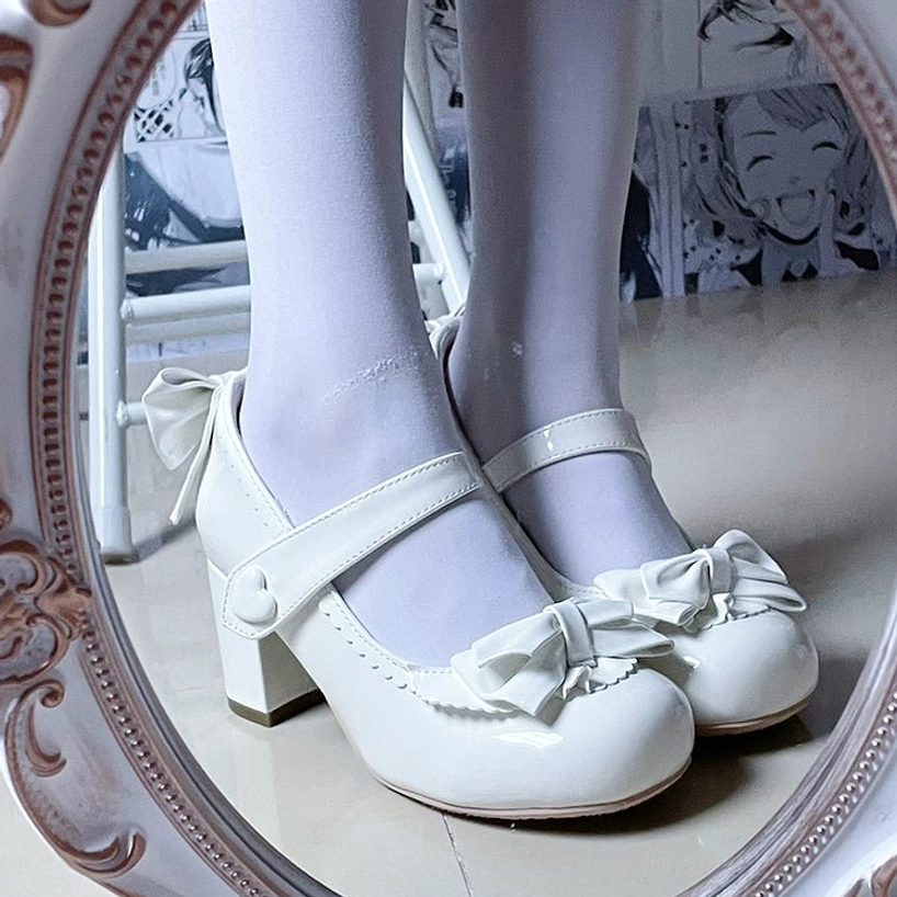 White patent leather Lolita Mary Jane high heels with front bow ornament scalloped edge heart-shaped buckle and chunky block heel shown in vintage carved mirror reflection with white stockings