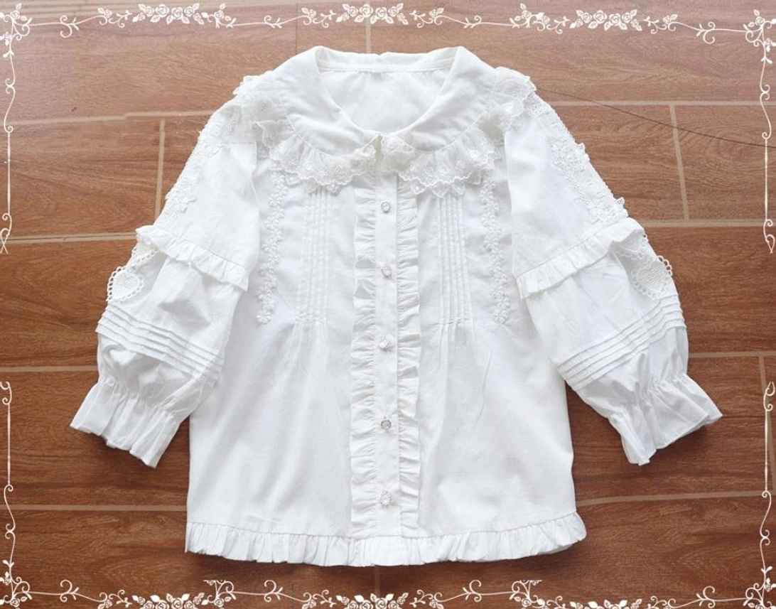 White sweet Lolita cotton blouse with Peter Pan collar, ruffled lace trim, and lantern sleeves in flat lay overhead view showcasing design details