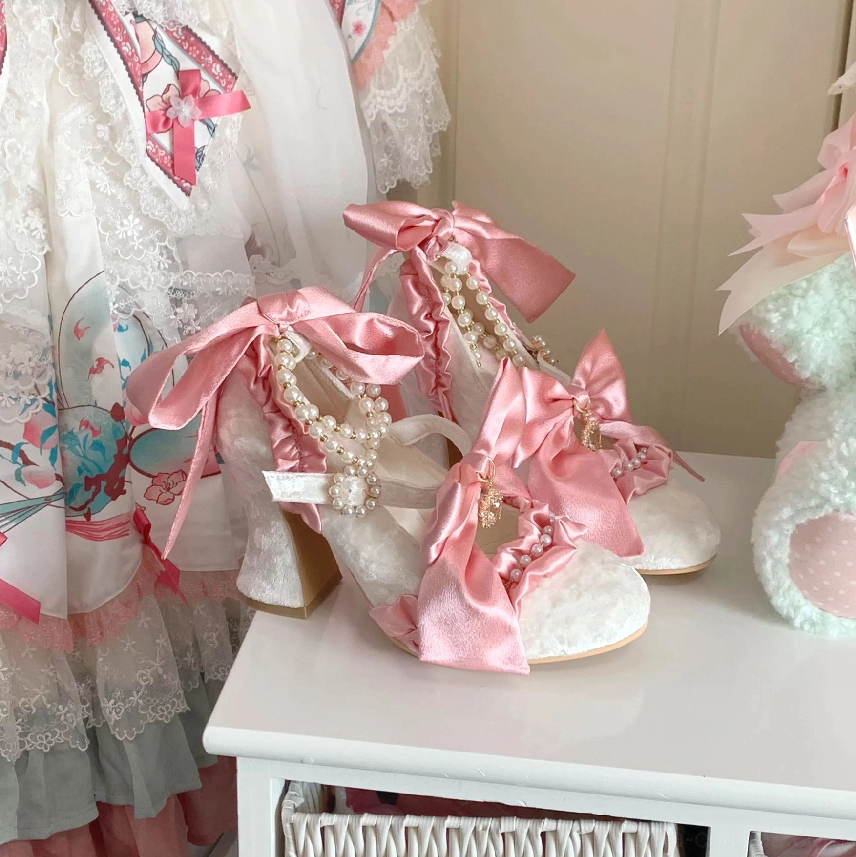 White satin upper pearl decorated lolita wedding heels with pink detachable bow on side table with matching dress and plush toy accessories