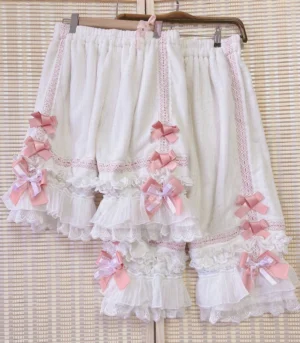 White lolita bloomers with pink satin bow accents featuring layered ruffled lace hem details and elastic waistband in flat hanging view